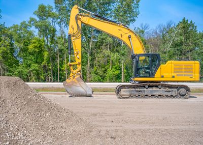 Yellow excavator on a dirt lot with trees in the background