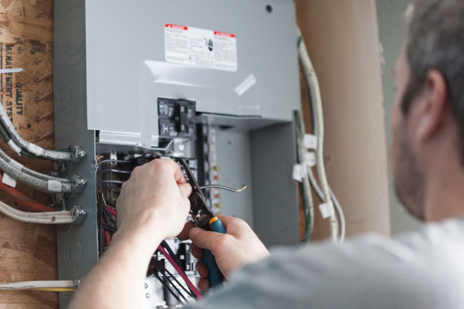 A man is working on an electrical box with a pair of pliers.