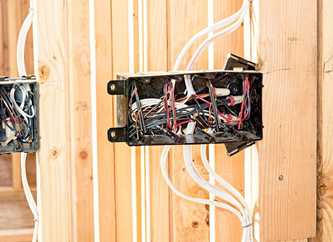 Electrical junction boxes with exposed wires installed on wooden framing.
