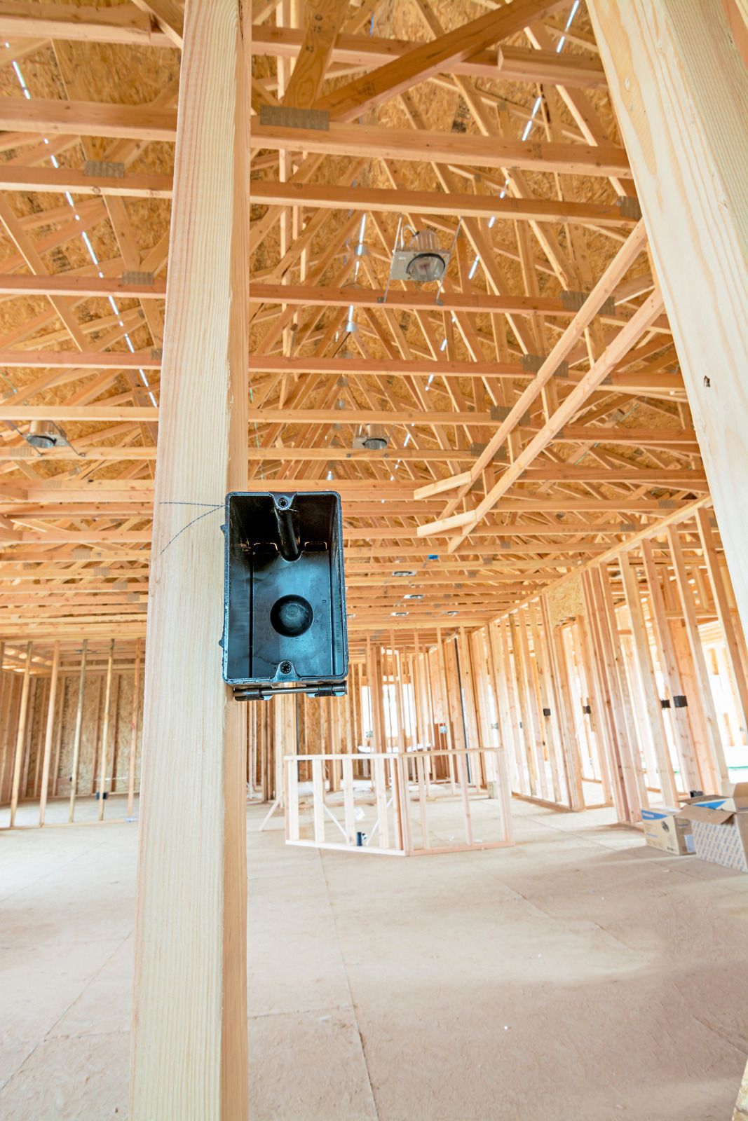 An electrical box is hanging from the ceiling of a house under construction.