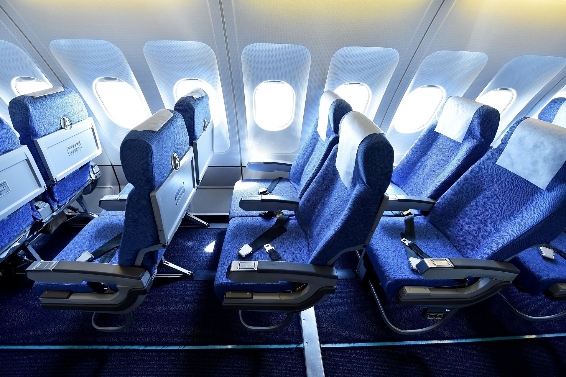 Airplane cabin interior with blue seats, overhead compartments, and windows.