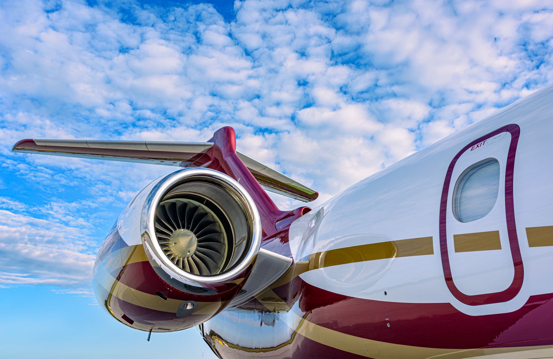Close-up of a burgundy and white private jet engine against a blue sky with clouds.