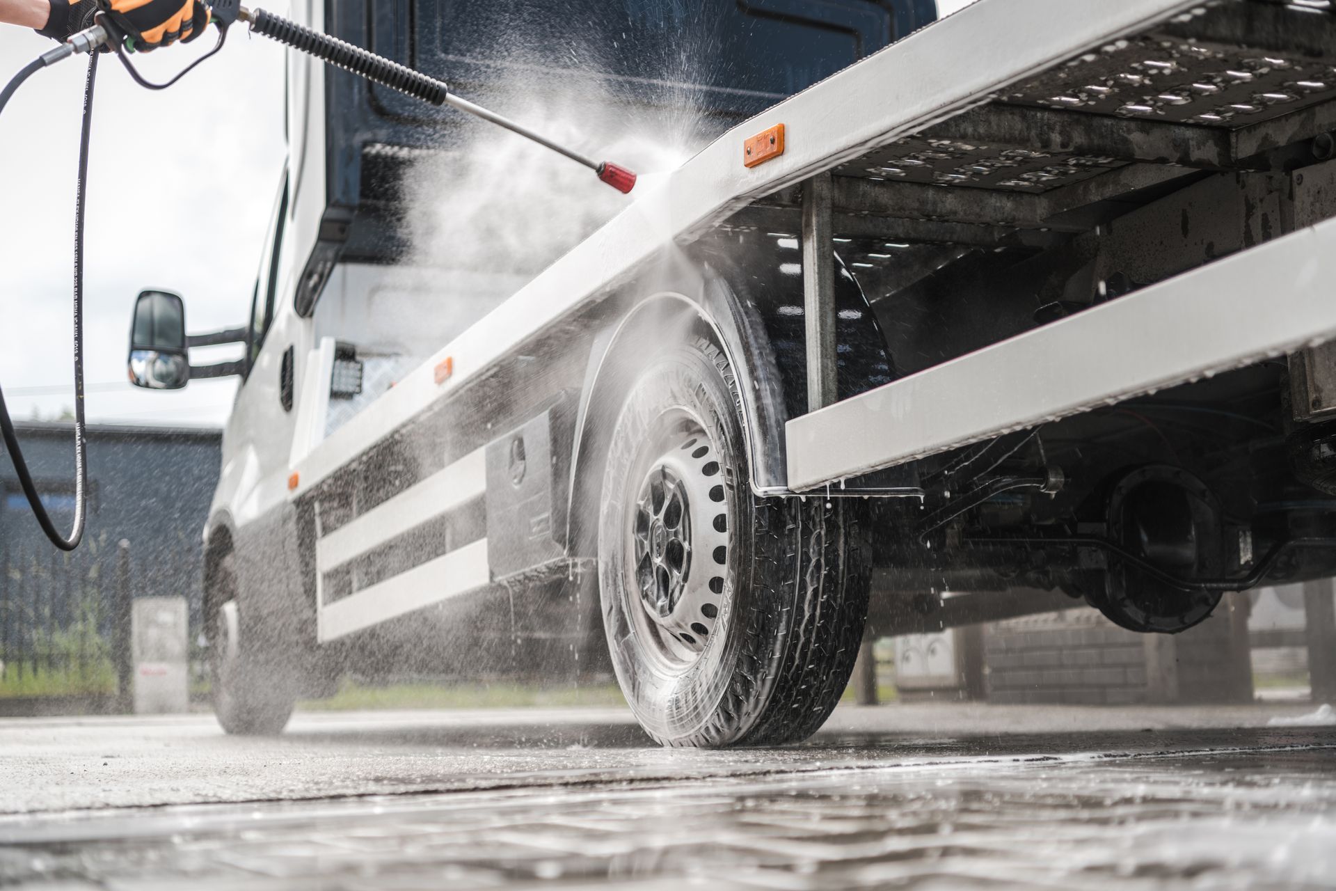 A person using a pressure washer to clean a tow truck on a concrete surface.