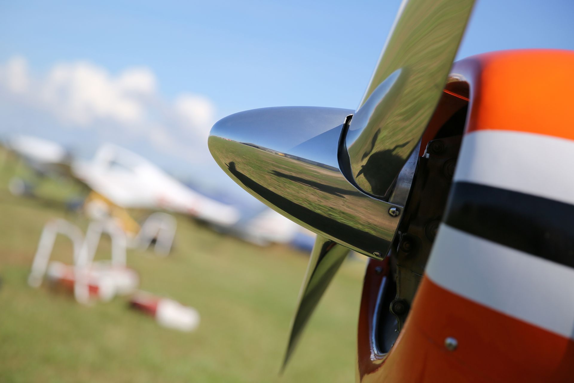 Airplane propeller, shiny metal blades, close-up, orange and white fuselage.
