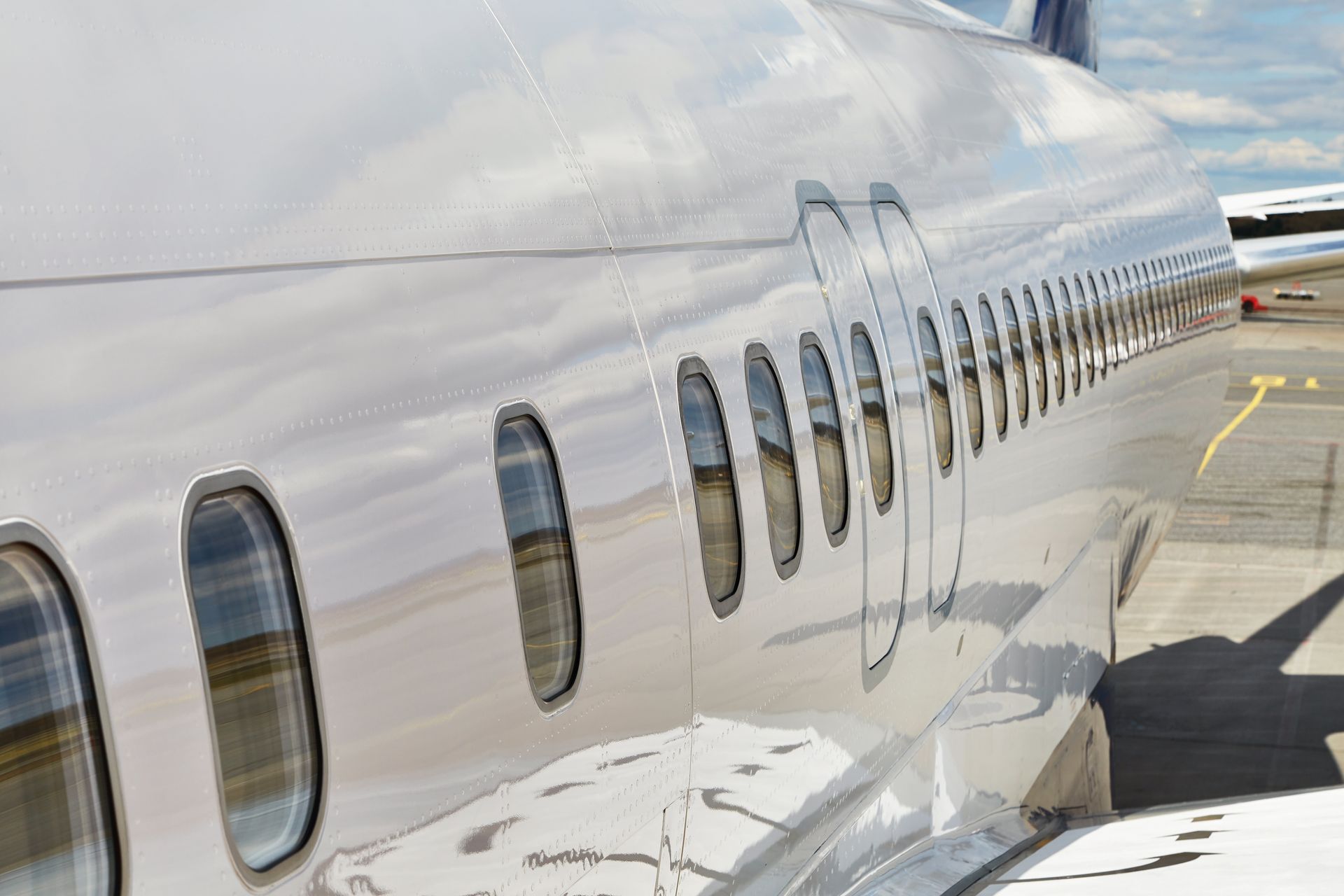 Side of a shiny white airplane with oval windows, parked on the tarmac.