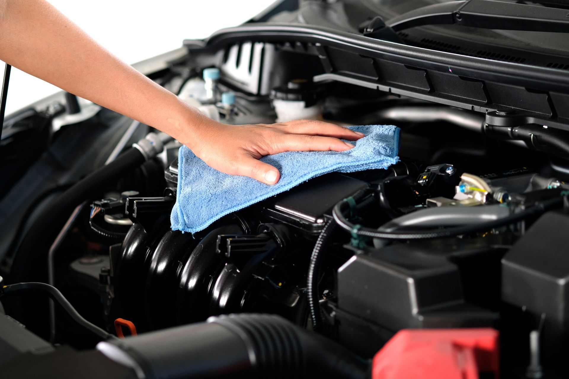 Person cleaning a car engine with a blue microfiber cloth.