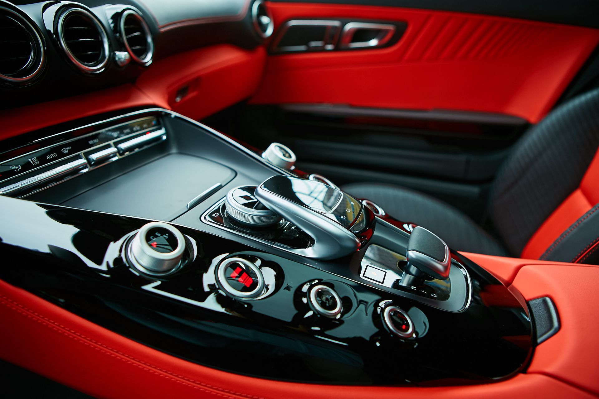 Black and red luxury car interior with glossy console, chrome gearshift, and red leather trim.