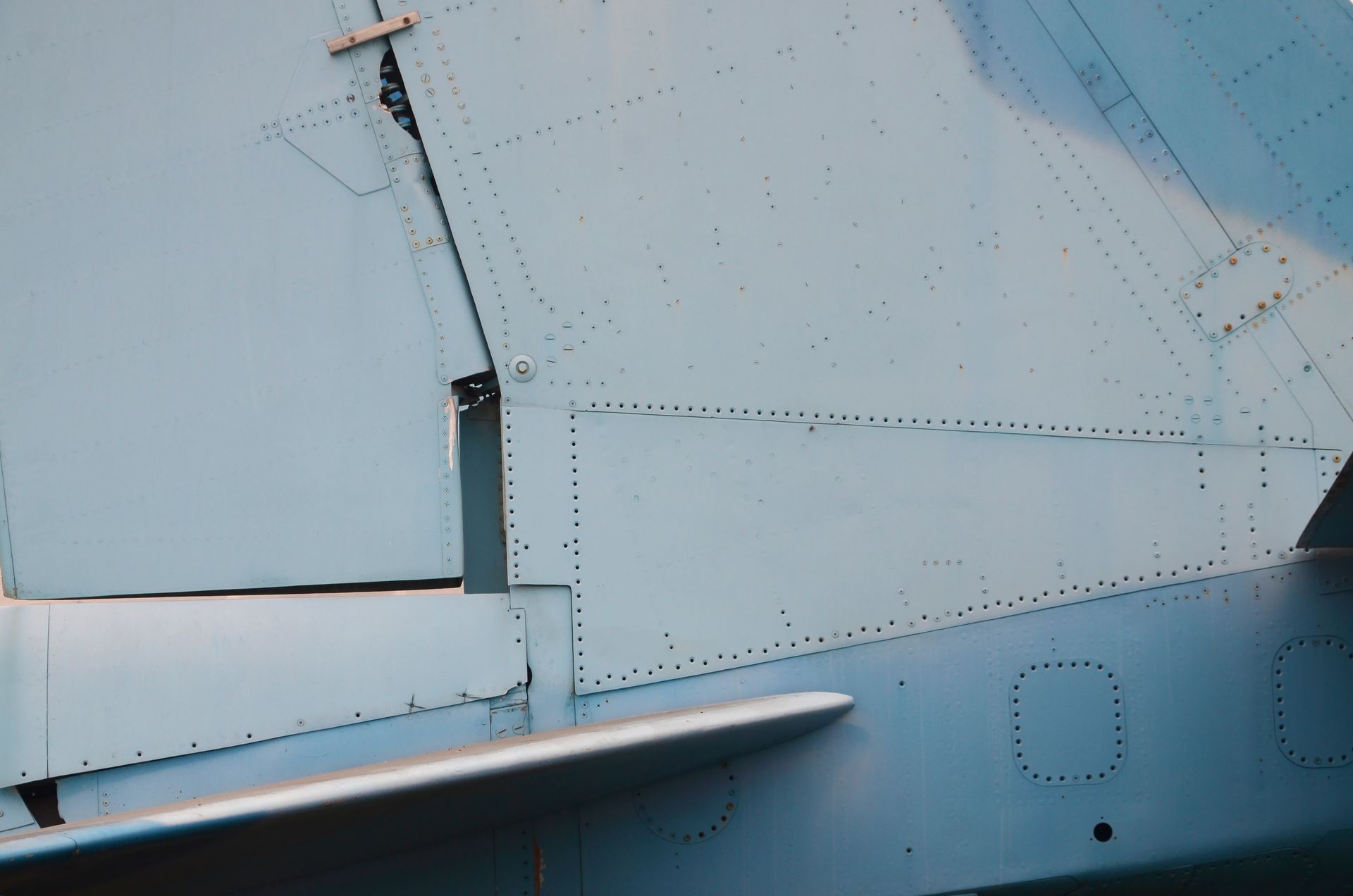 Close-up of a blue aircraft's tail section, showing riveted metal panels and a vertical fin.