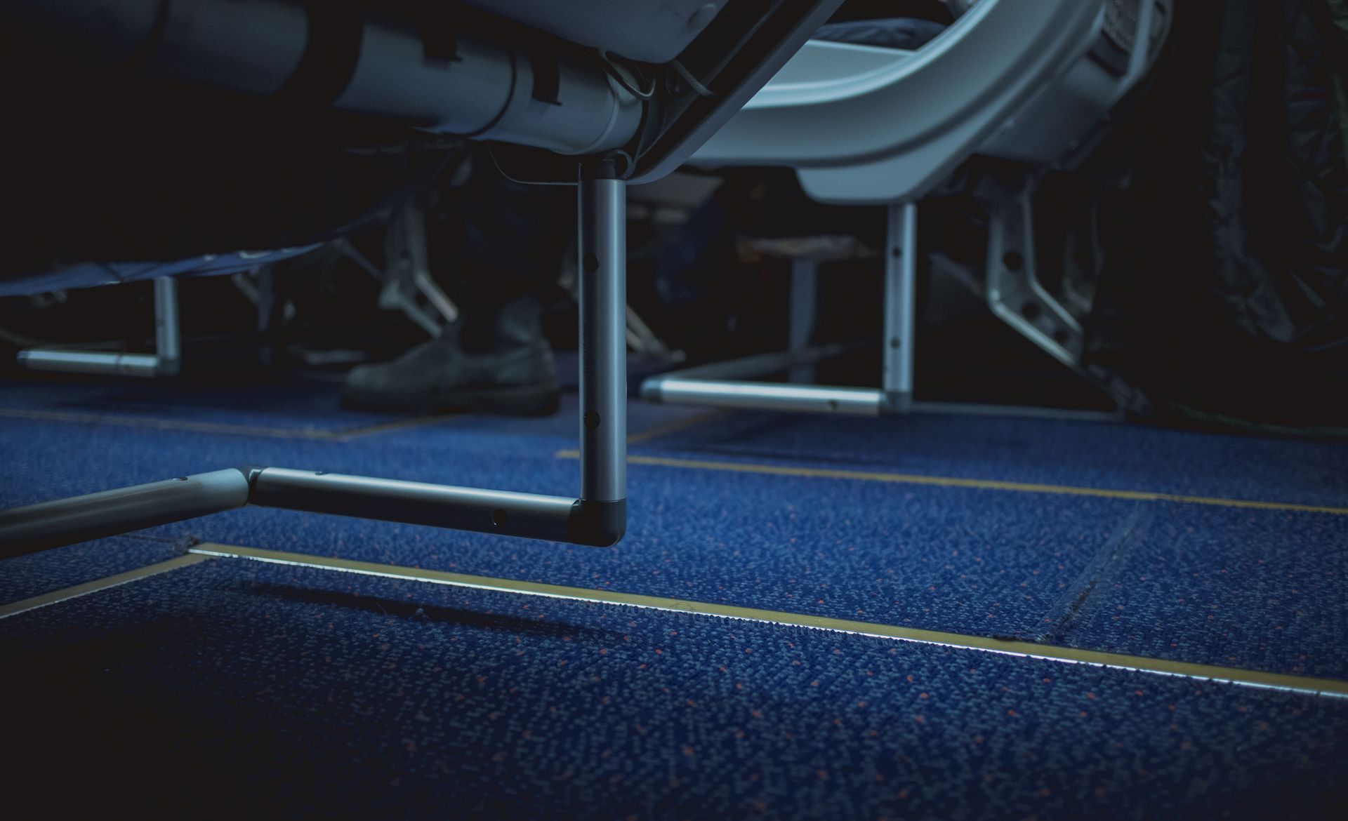 Low-angle view of a vehicle interior: blue carpet, metal supports, and passenger feet are visible.