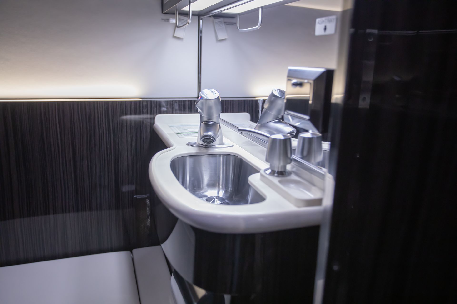 An airplane lavatory with a stainless steel sink, faucets, and a paper towel dispenser.