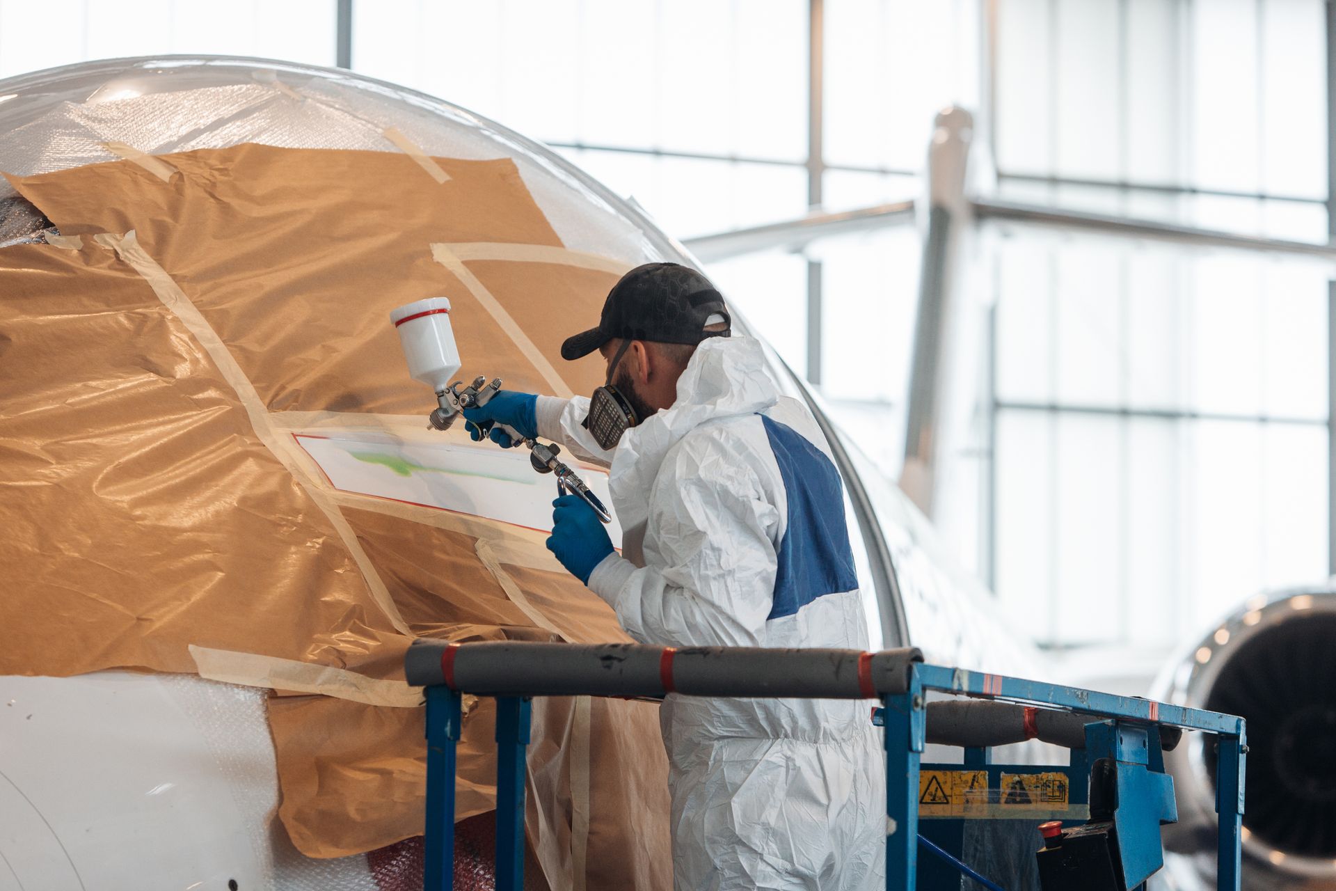 Person in protective suit painting a plane with a spray gun, using a lift.