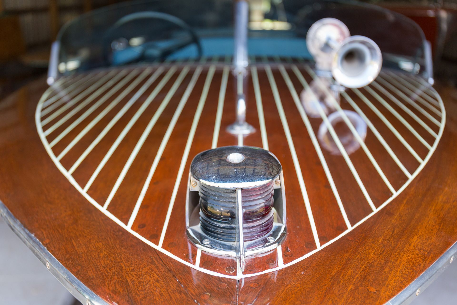 Close-up of a classic wooden boat's bow, showing wood grain, chrome accents, and a horn.