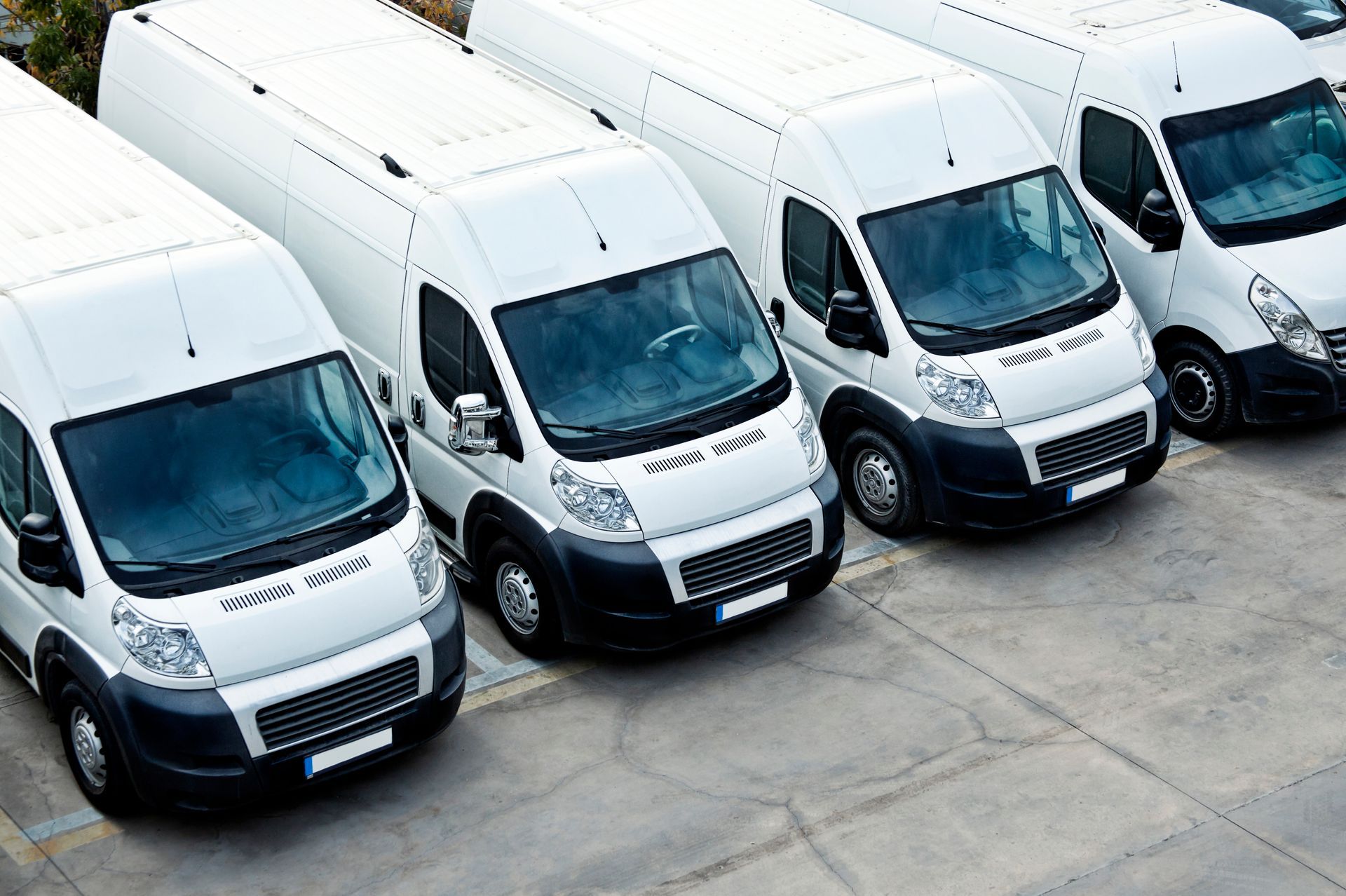 Four white vans parked in a row on a concrete surface.