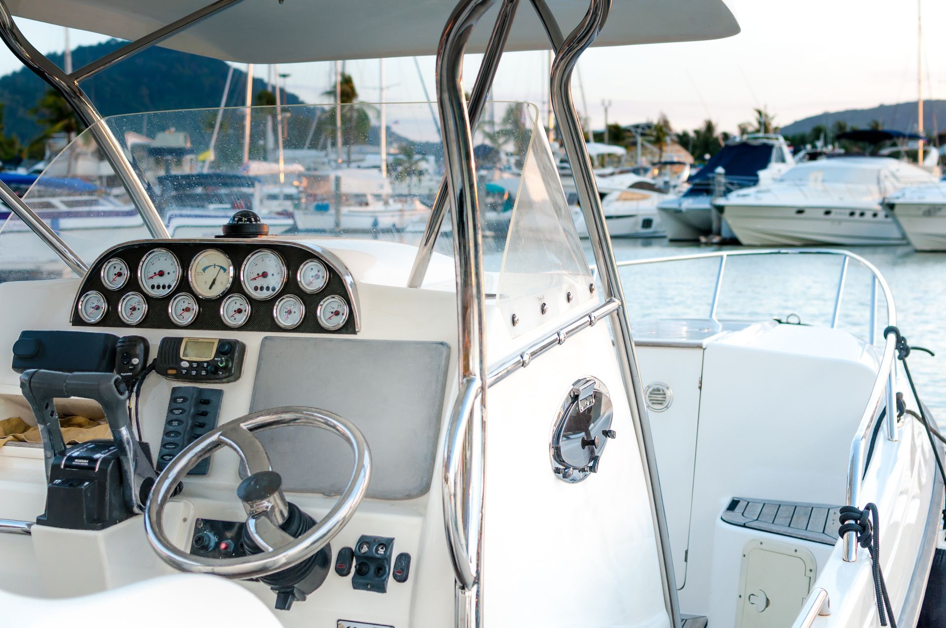 Boat dashboard with gauges and steering wheel, overlooking harbor with other boats.