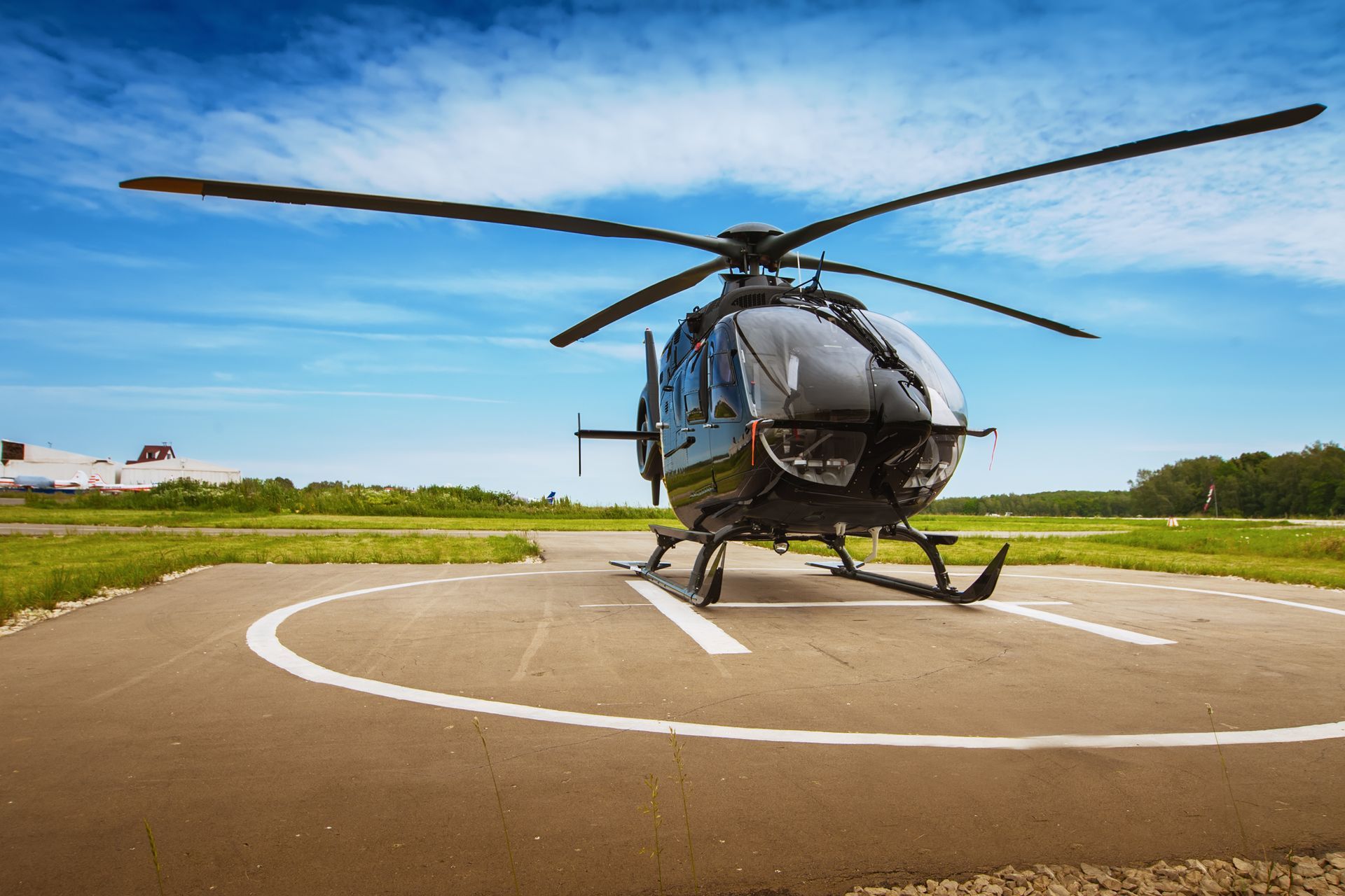Black helicopter on a helipad against a blue sky, ready for flight.
