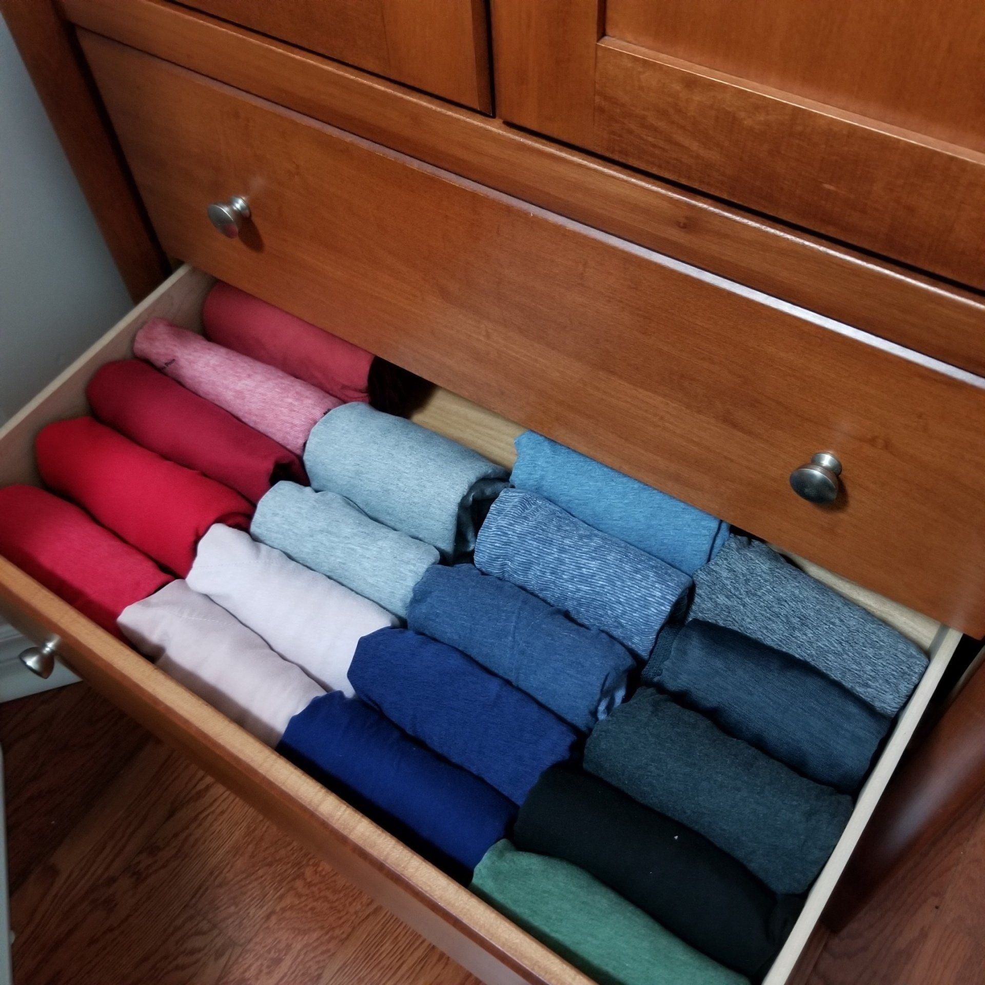 A drawer filled with rolled up shirts of different colors