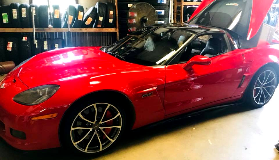 A bright red Chevrolet Corvette with an open trunk parked inside a tire shop.