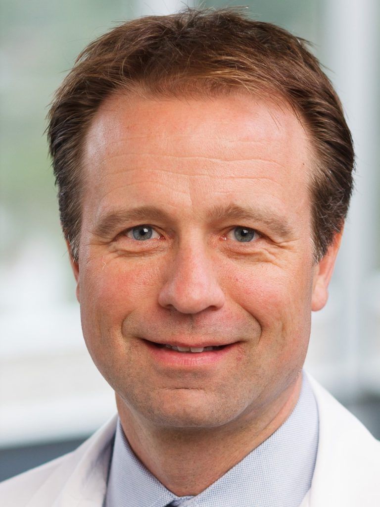 A man in a white coat and tie is smiling for the camera