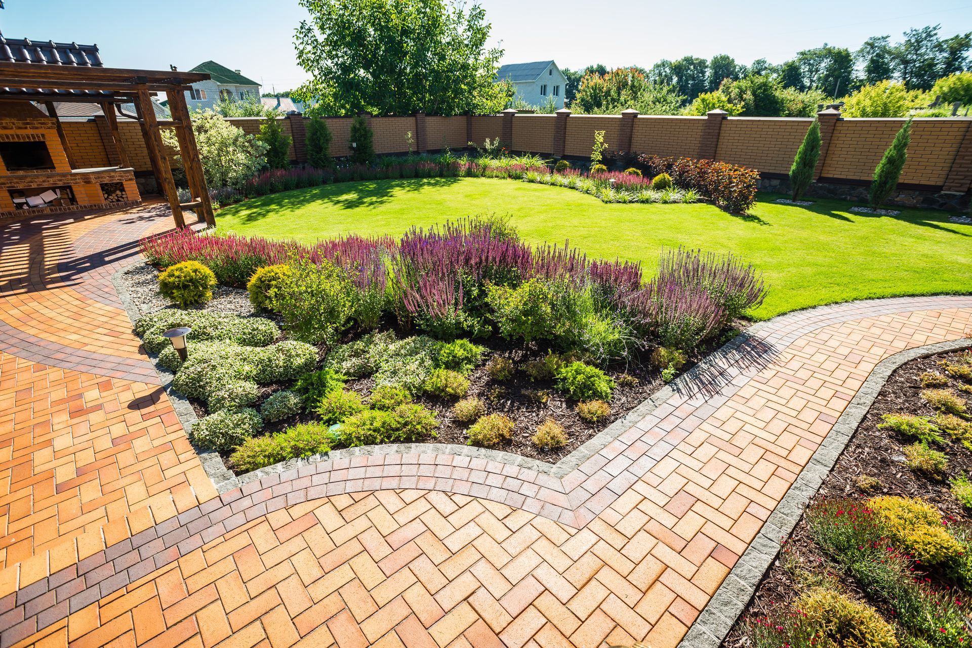 Lush backyard with brick pathways, flower beds, green lawn, and wooden pergola.