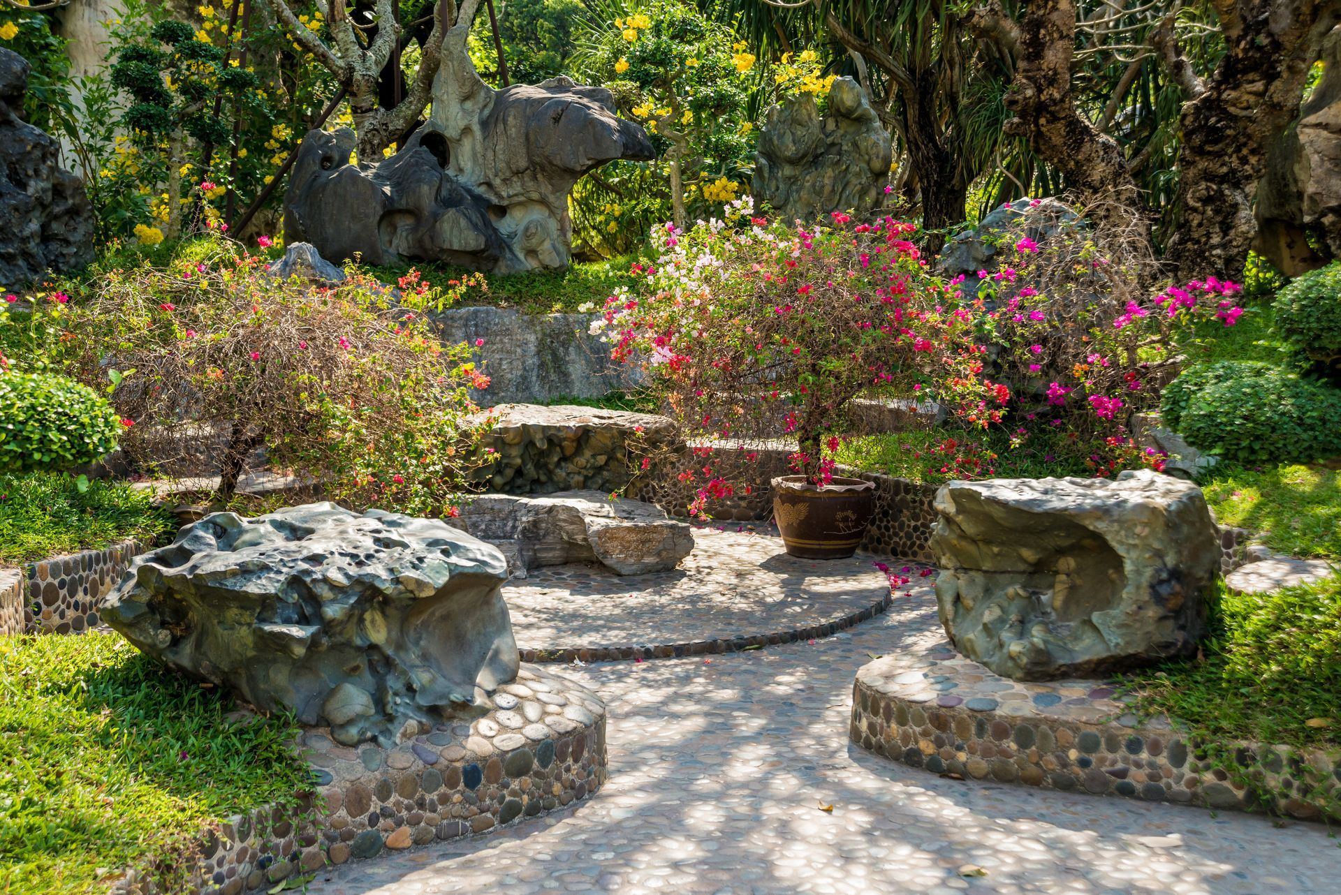 Stone garden with plants and flowers, featuring large rock seating and winding pathways.