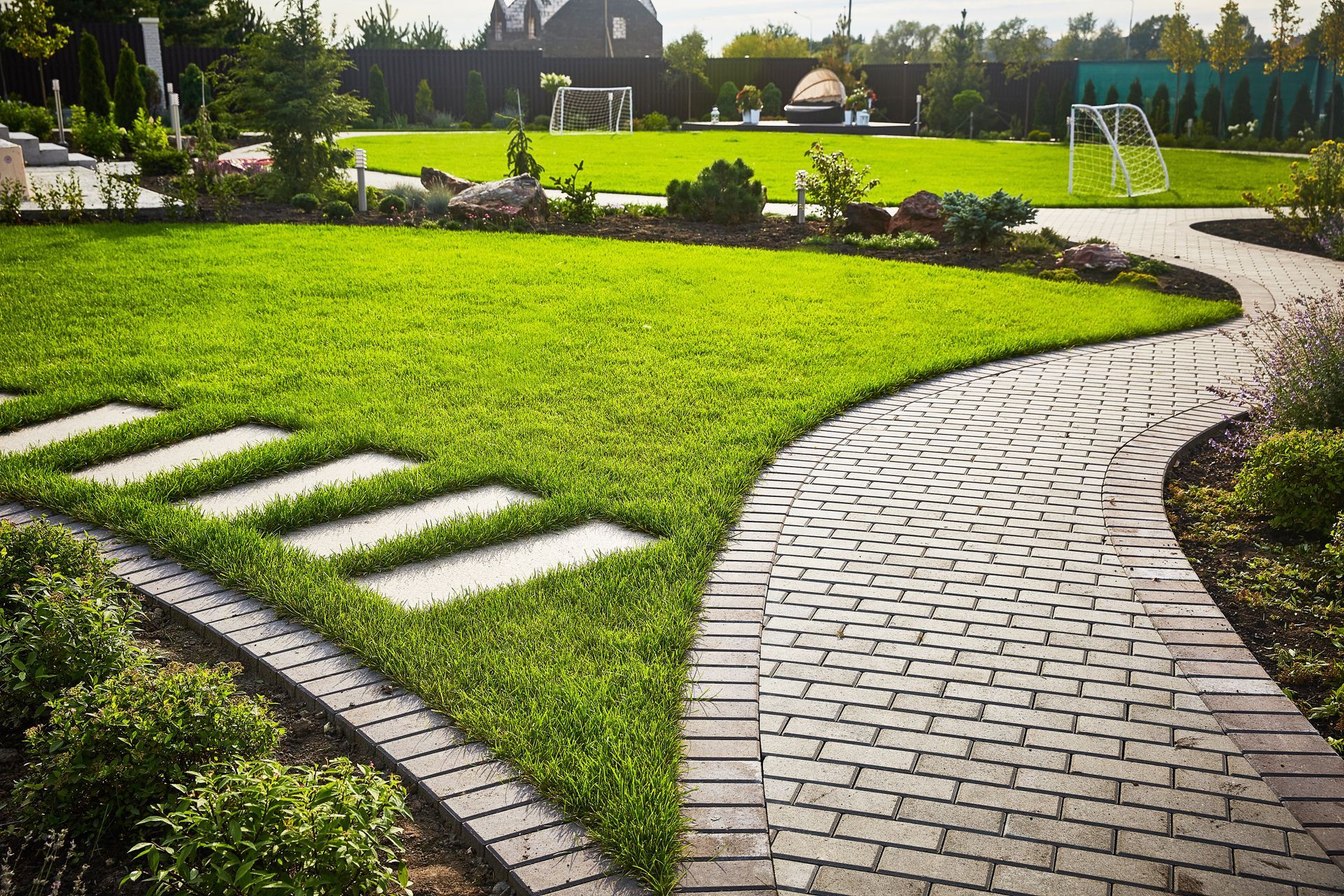 Curving paved path through green lawn, leading to a grassy backyard with soccer goals.