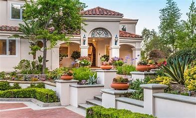 Exterior of a two-story home with a manicured front yard, flower pots, and steps leading to the entrance.