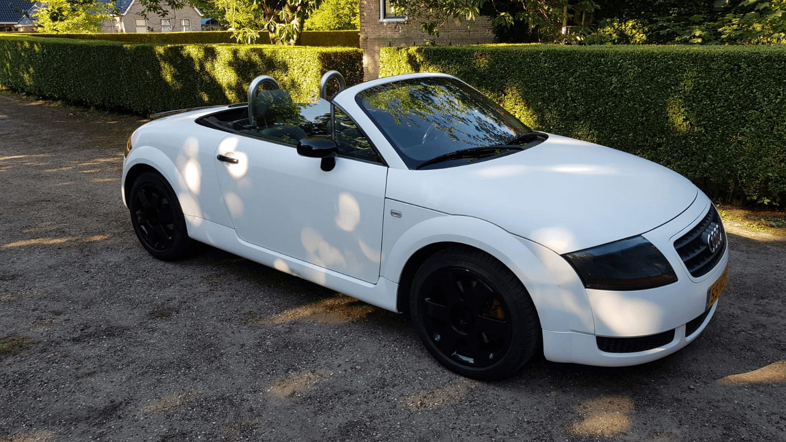 Een witte cabriolet staat geparkeerd op een grindpad