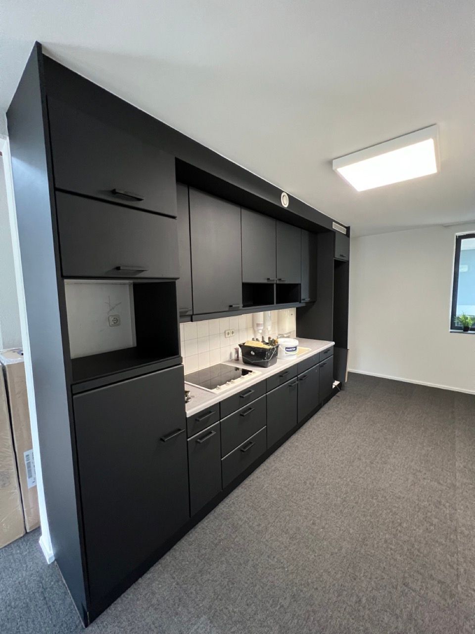 Een keuken met zwarte kasten, een gootsteen en een raam.