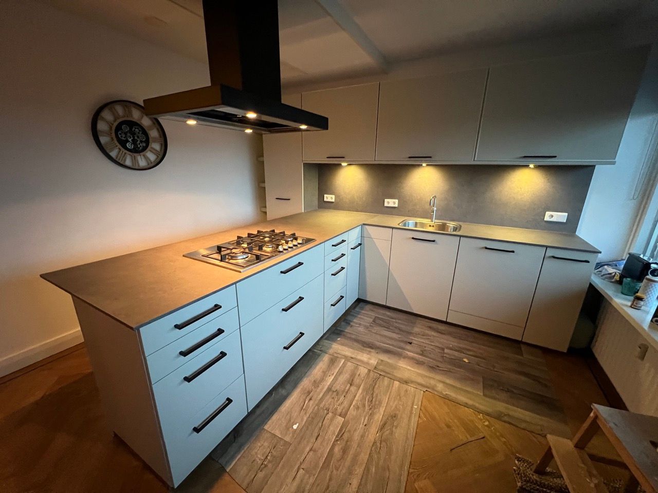 Een keuken met witte kasten, een kookplaat, een oven, een gootsteen en een klok aan de muur.