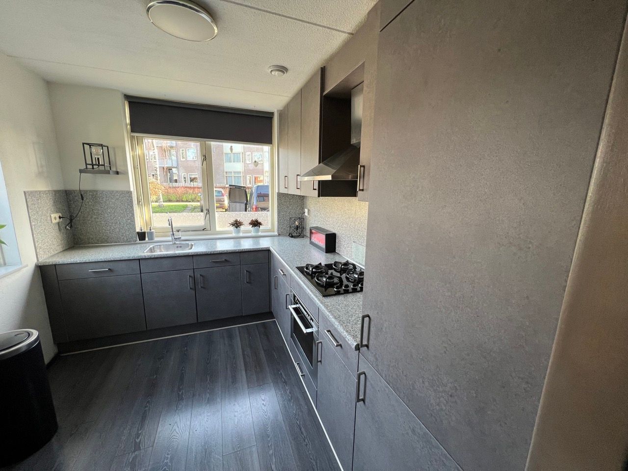 Een keuken met grijze kasten, een fornuis, een gootsteen en een raam.