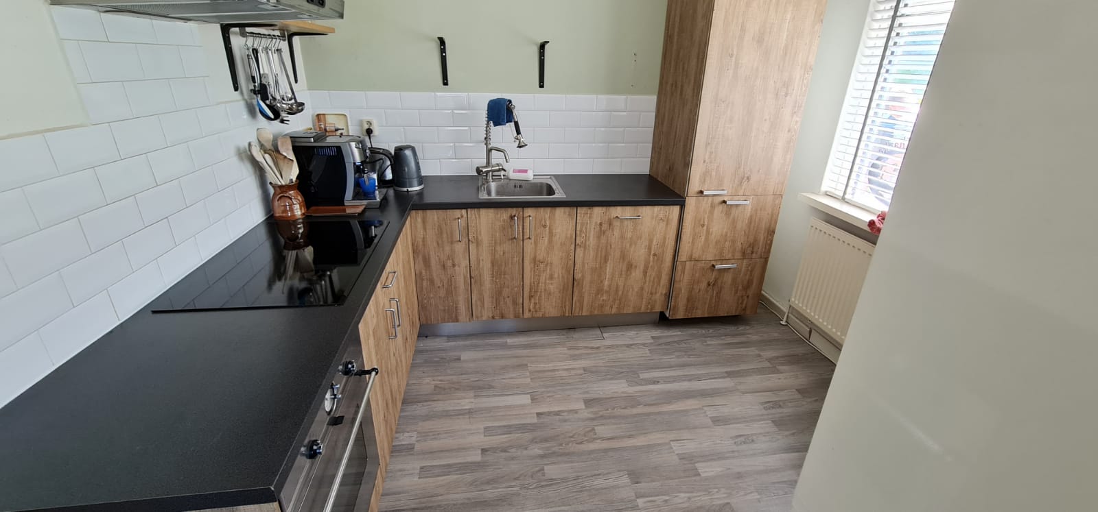 Een keuken met een fornuis, gootsteen, kasten en een raam.