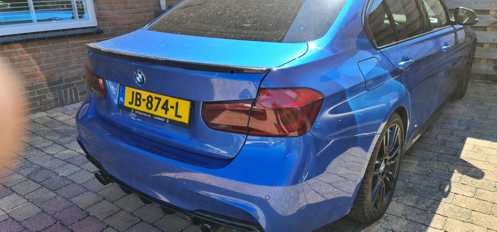 Een blauwe bmw met een kentekenplaat waarop jb-874-l staat, staat geparkeerd op een oprit.