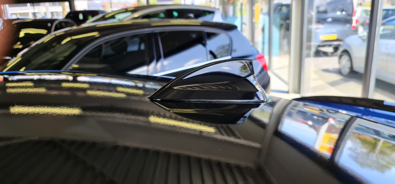 Een zwarte auto staat in een showroom geparkeerd naast een andere auto.