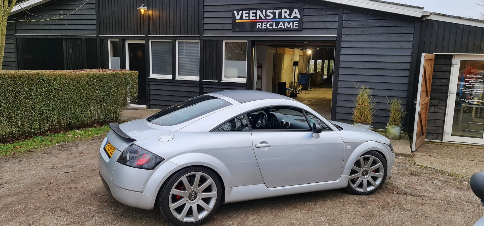 Een zilveren auto staat geparkeerd voor een zwart gebouw.