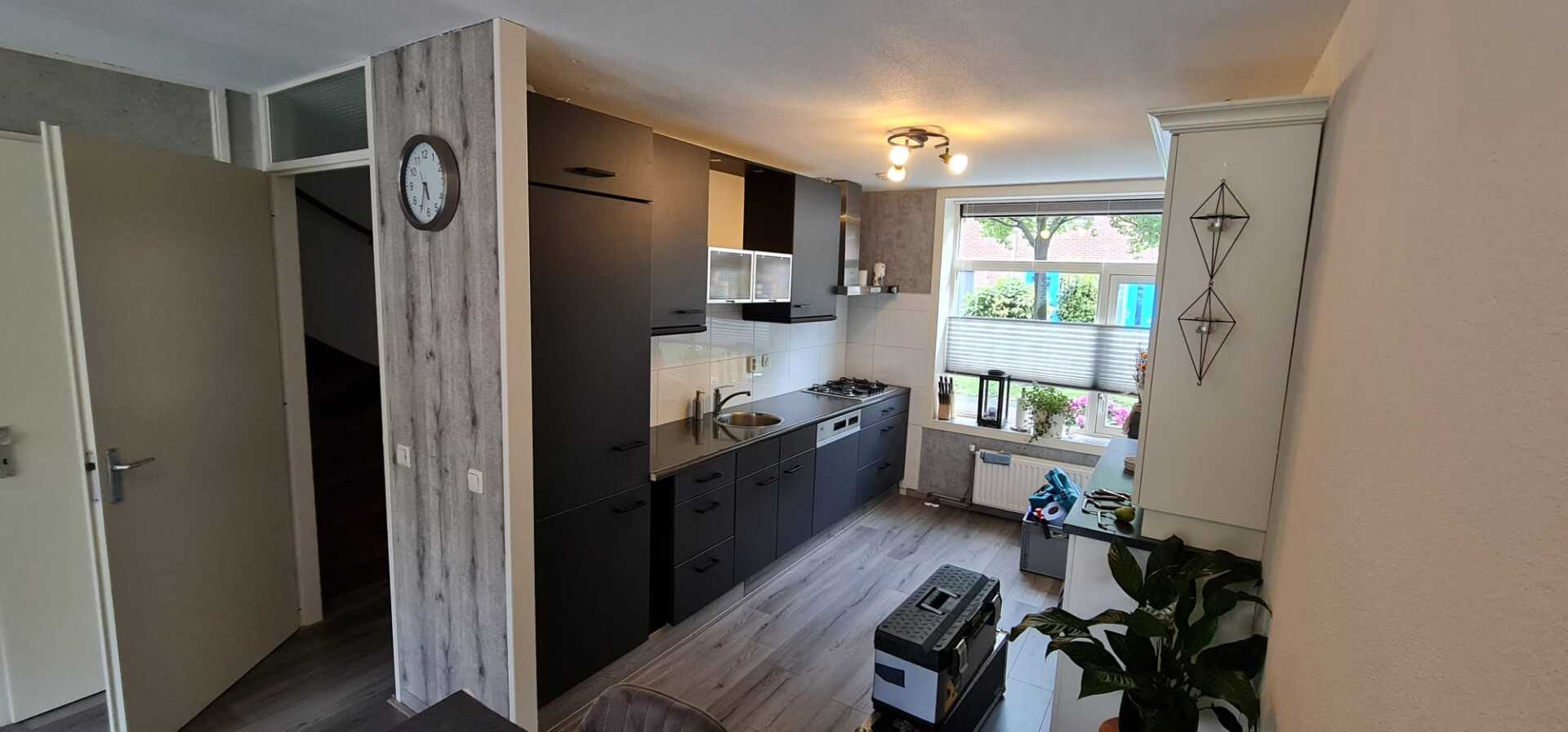 Een keuken met zwarte kasten en een klok aan de muur.