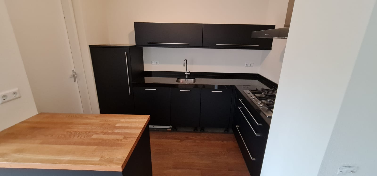 Een keuken met zwarte kasten en een houten aanrechtblad