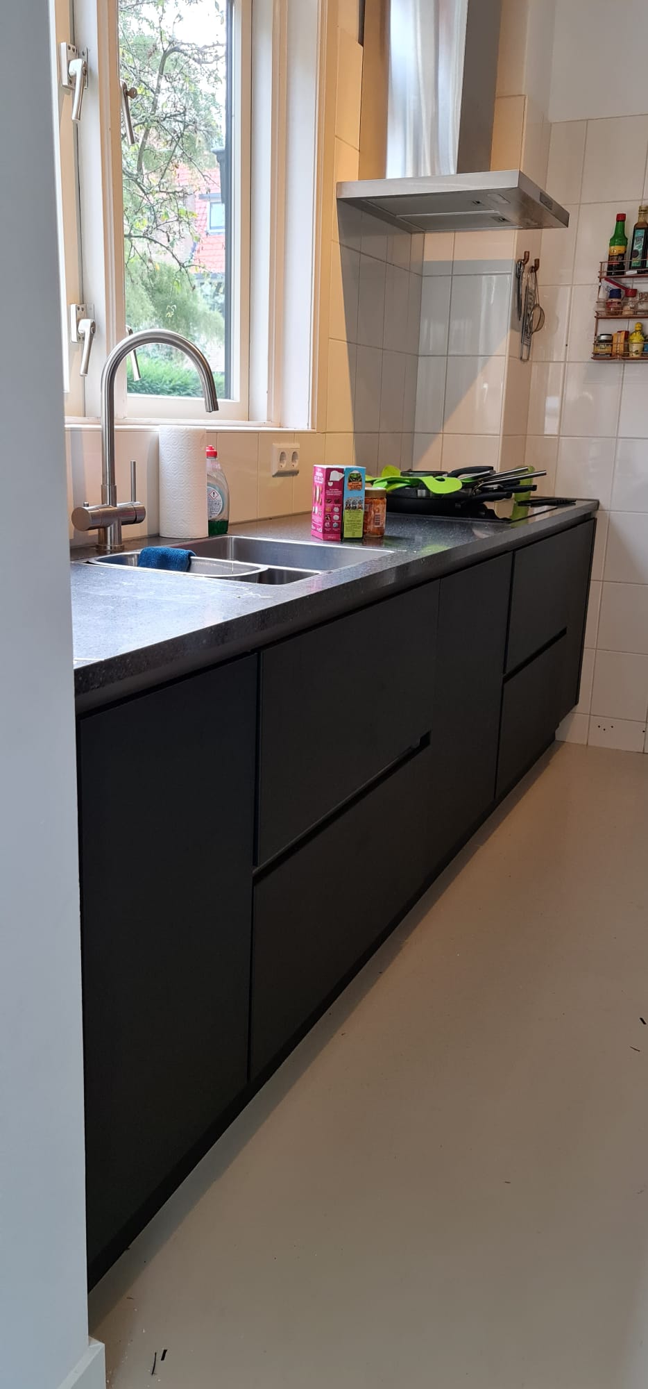 Een keuken met zwarte kasten, een gootsteen en een raam.