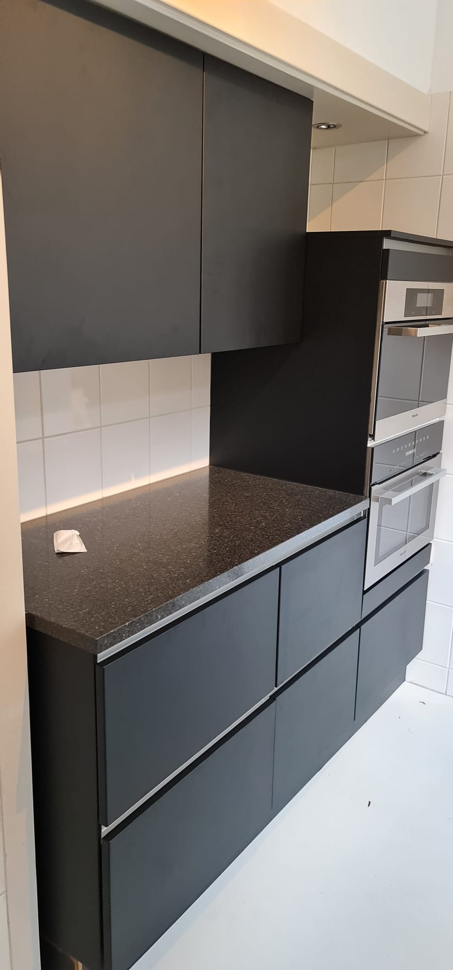 Een keuken met zwarte kasten, granieten aanrechtbladen en roestvrijstalen apparatuur.