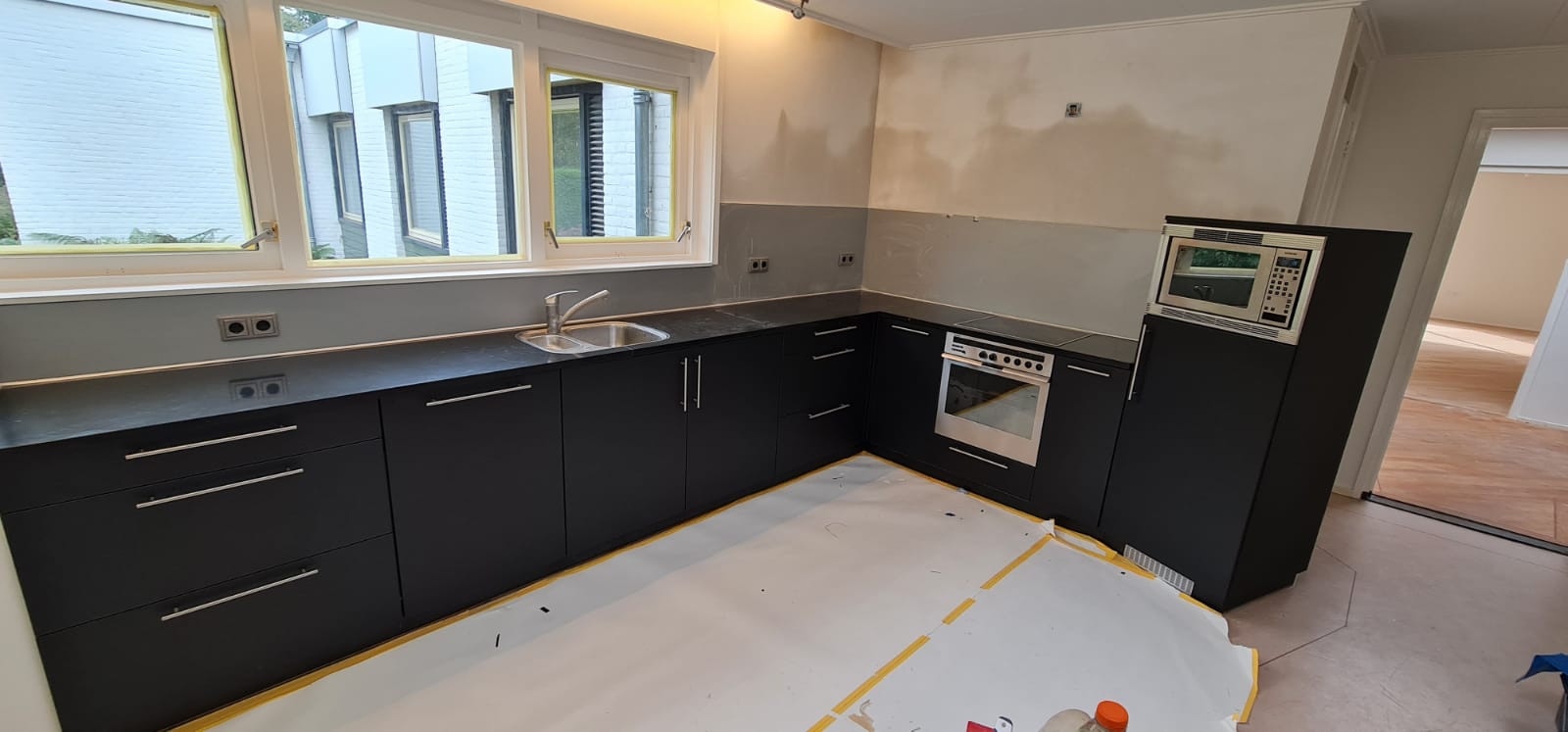 Een keuken in aanbouw met zwarte kasten en een fornuis.