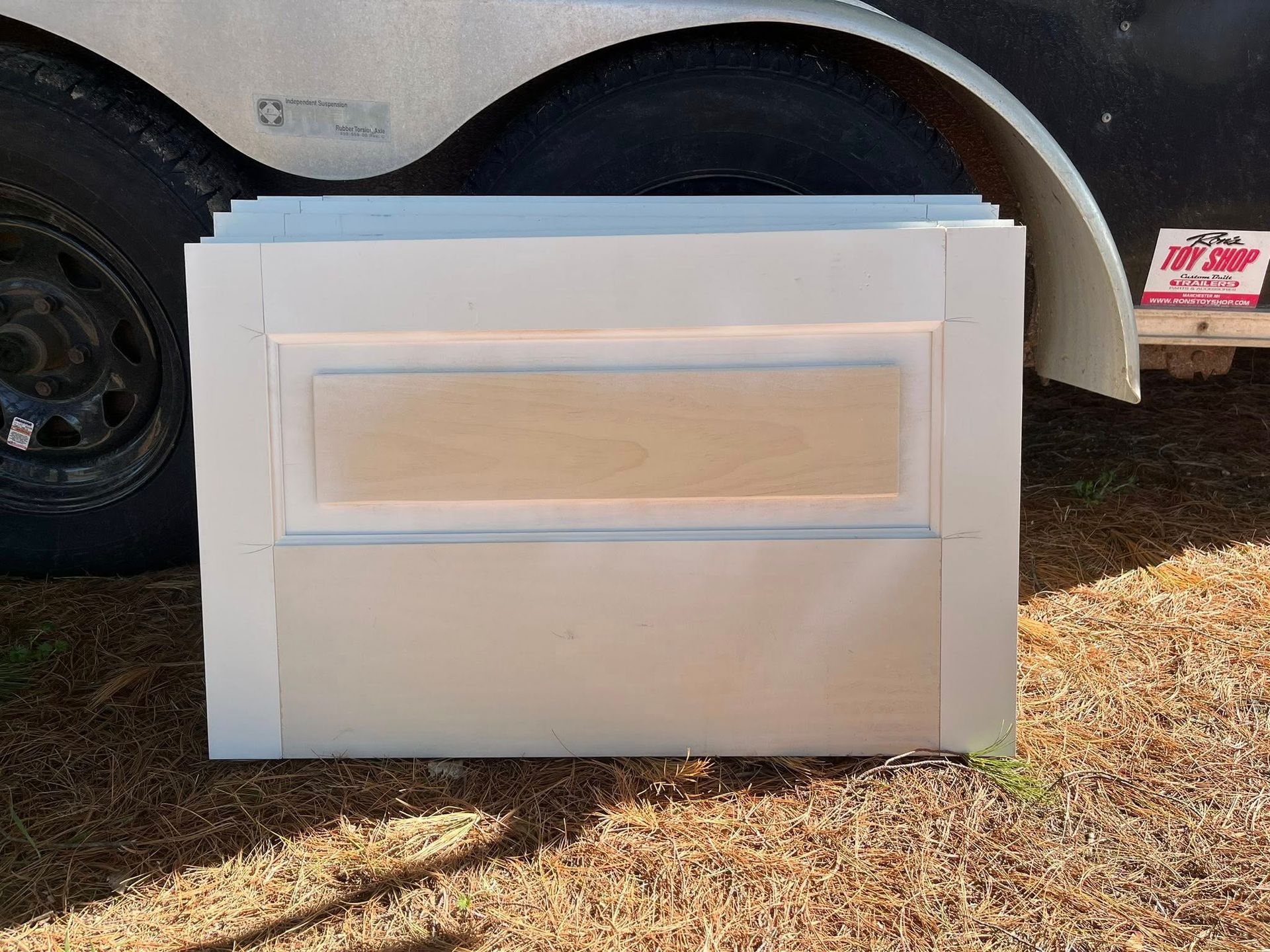 A stack of unfinished, rectangular cabinet doors with white-painted frames and raw wood center panels outdoors.