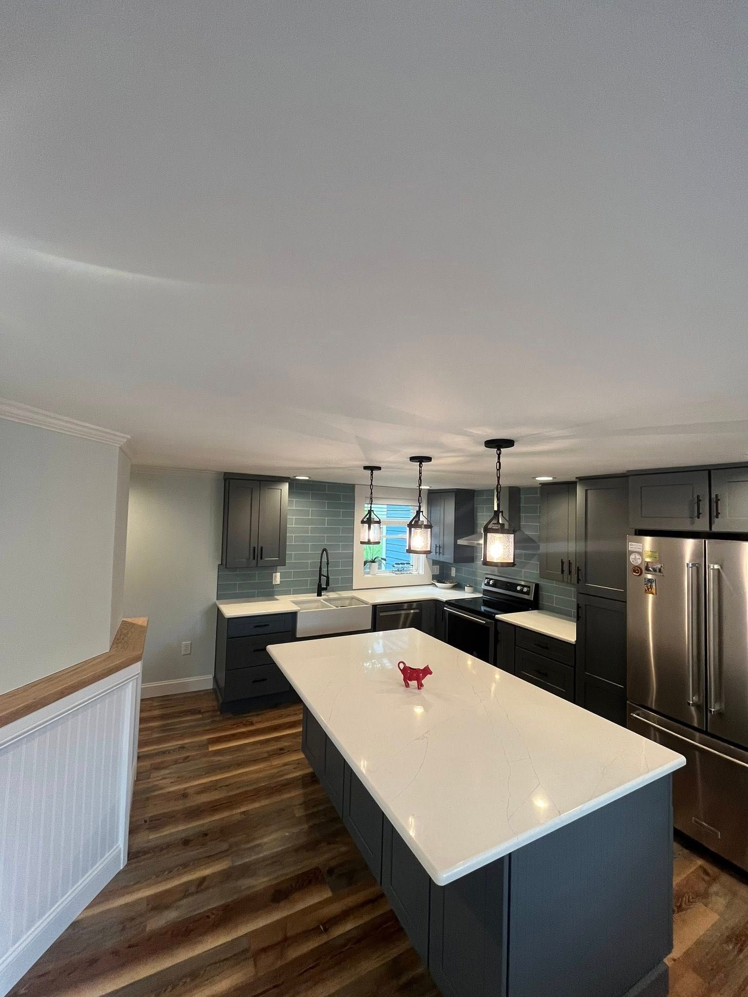 Modern kitchen with a dark-grey island, white countertops, stainless steel appliances, and wood-grain flooring.