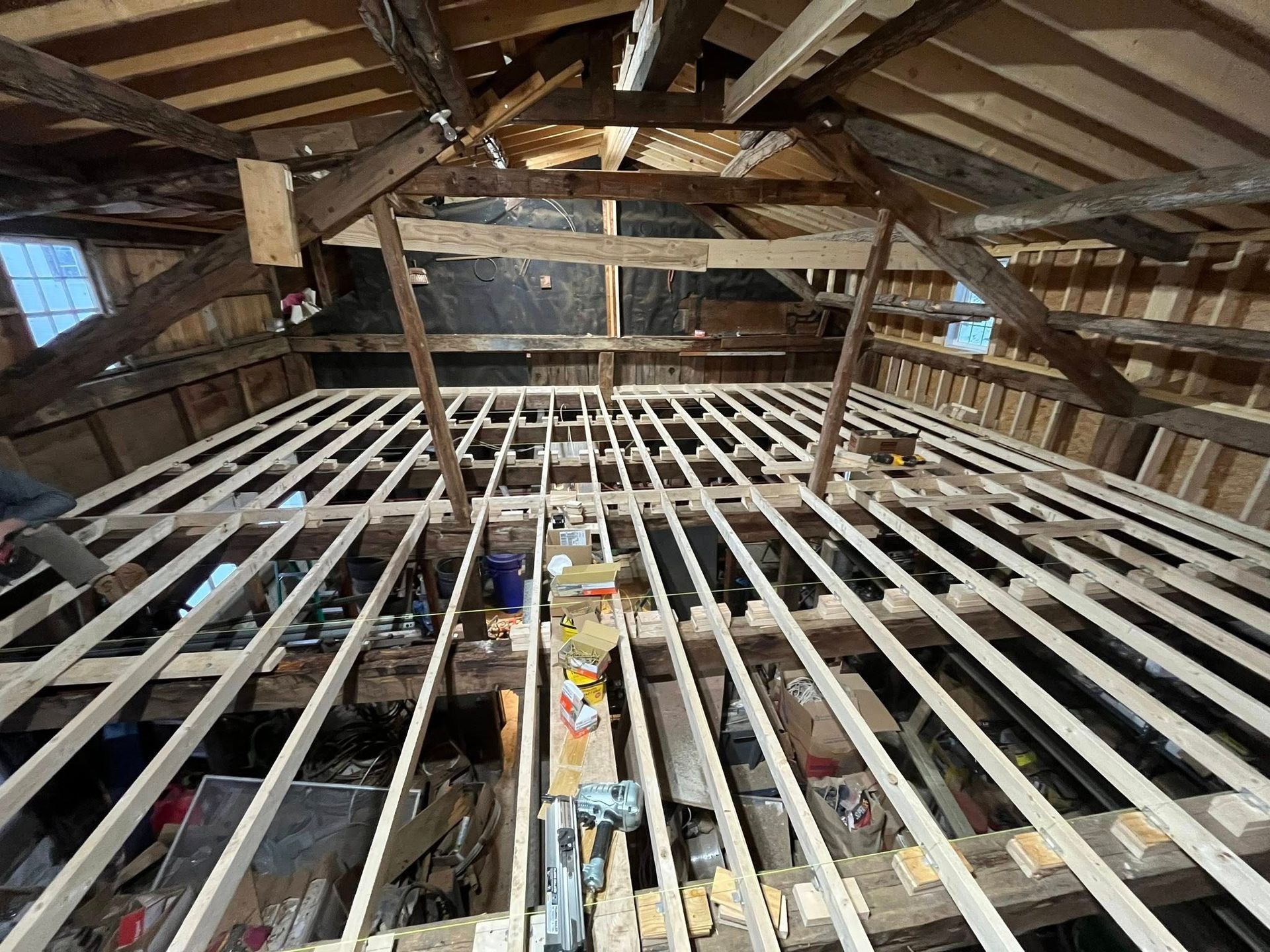 Unfinished wooden floor joists installed in an attic space with exposed wooden rafters and beams.