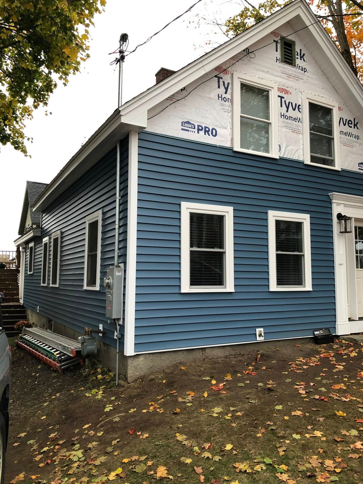 A blue-sided house with partially installed siding, exposed white building wrap, and an exterior electrical service panel.