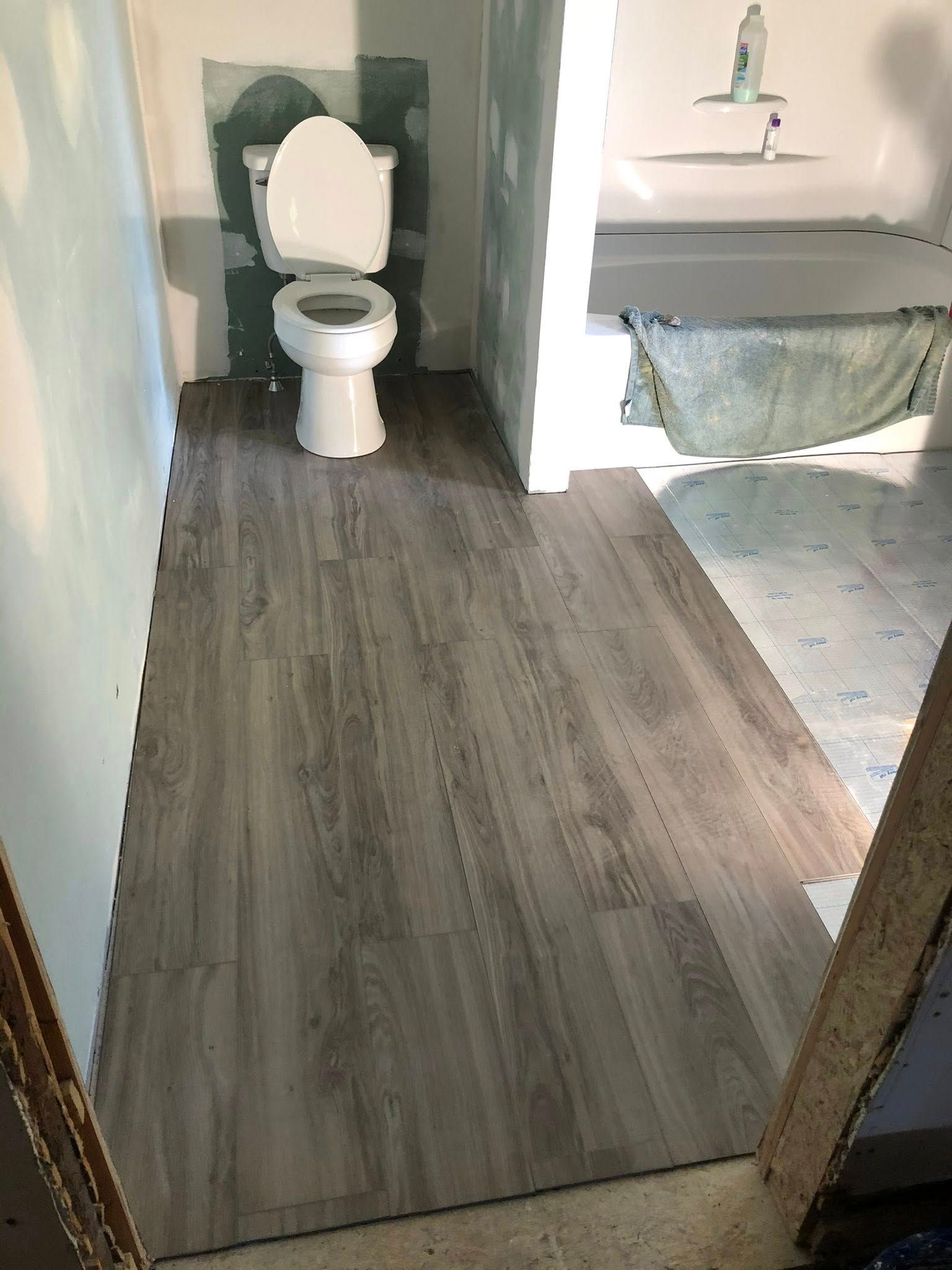 A bathroom under construction with new wood-look vinyl plank flooring partially installed next to an old tiled floor.
