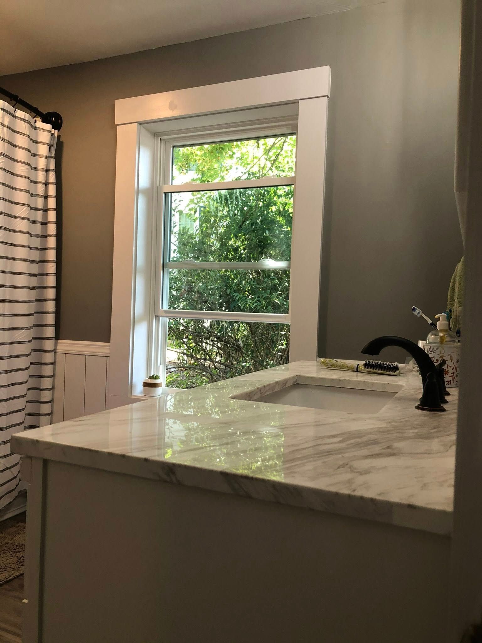 A bathroom with a marble countertop, black faucet, and a window with white trim, set against gray walls.