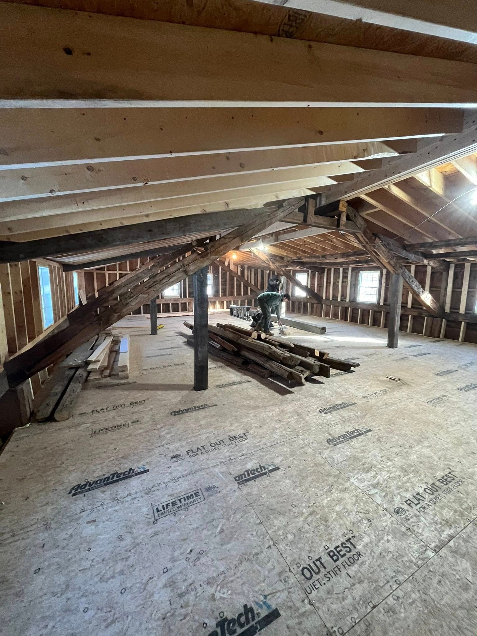 An unfinished attic interior with exposed wooden framing, structural support posts, and plywood subflooring.
