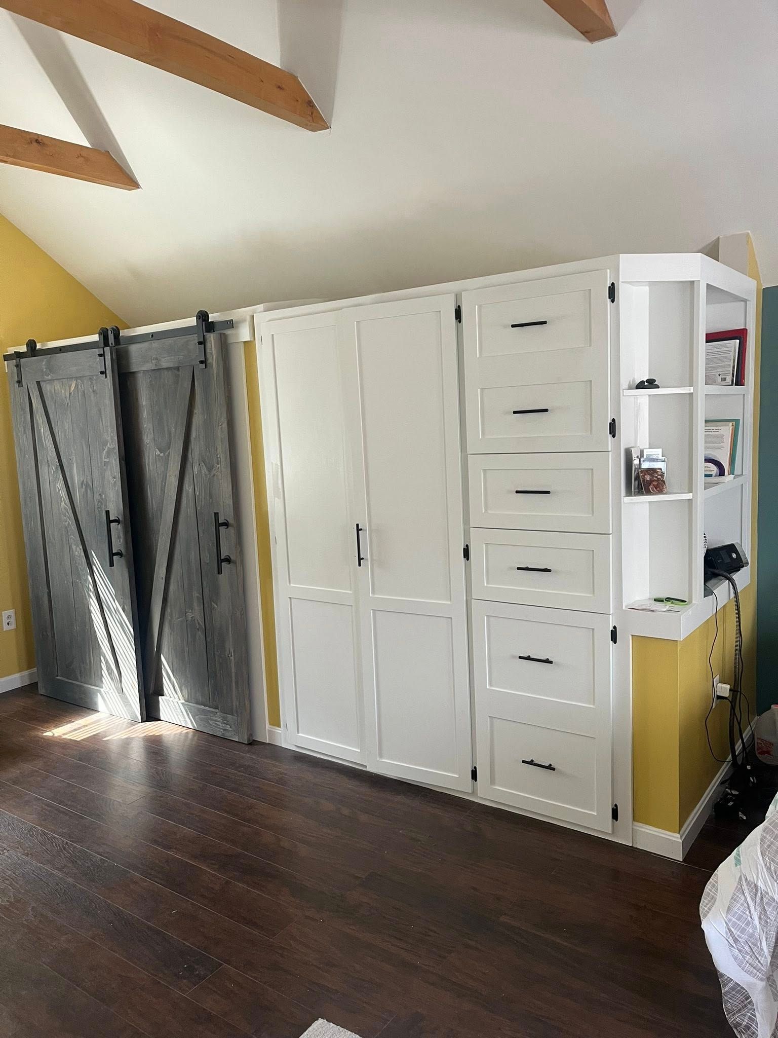 A white built-in storage unit with drawers and shelving next to sliding barn doors against a yellow wall.