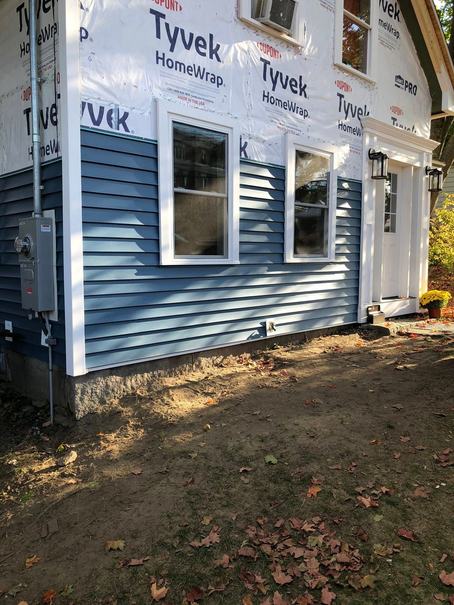 A side view of a house under renovation with blue horizontal siding installed over white Tyvek weather-resistant barrier.