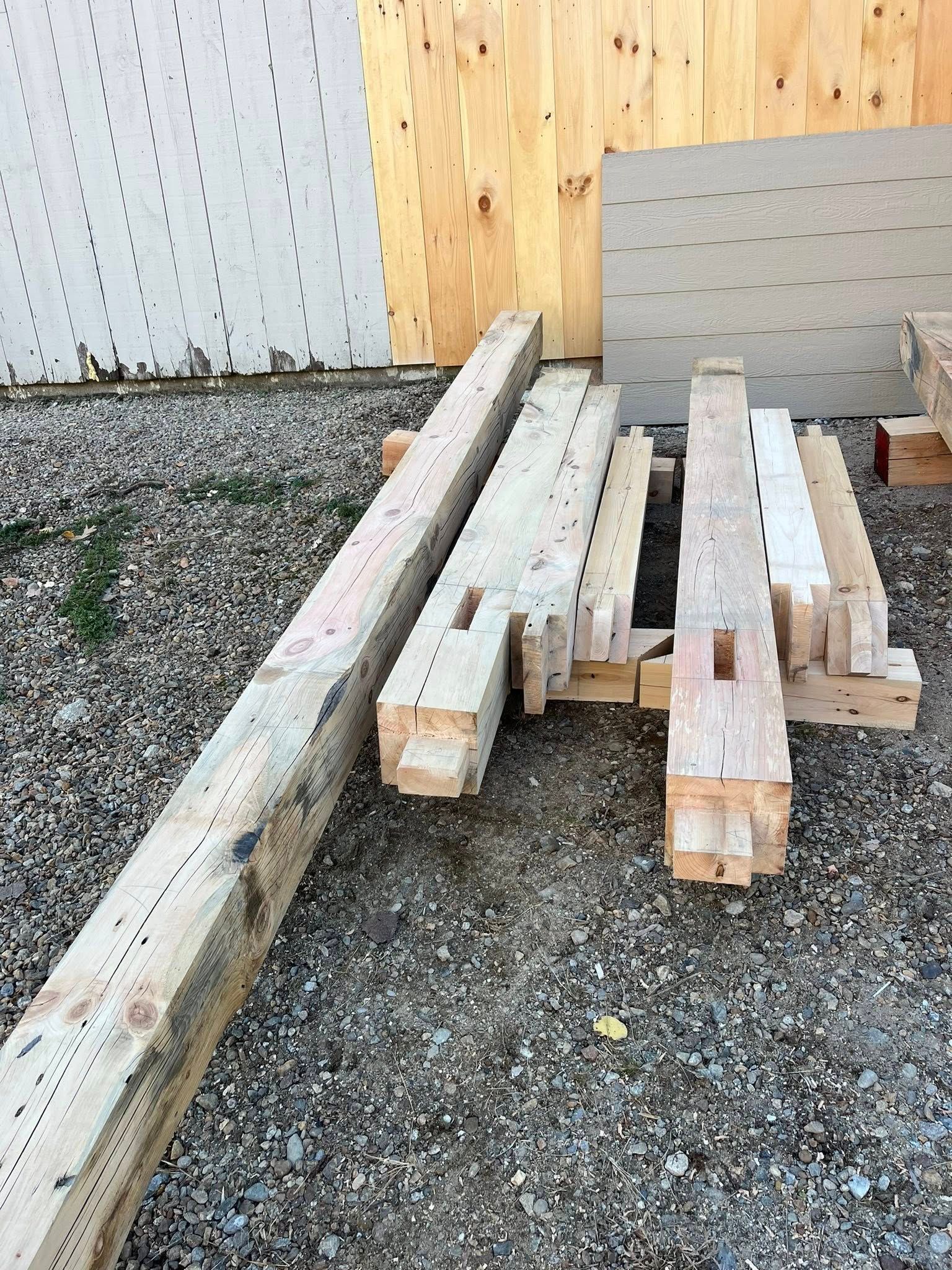 Several wooden beams with mortise-and-tenon joints laid out on a gravel surface.