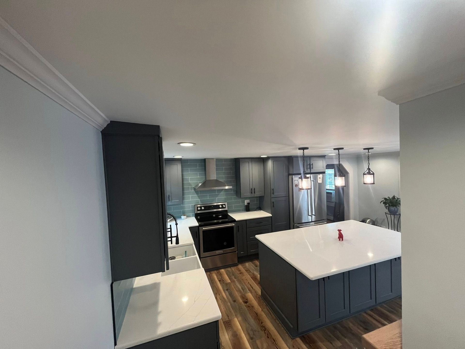 A modern kitchen with dark grey cabinets, a large white kitchen island, and wood-patterned flooring.